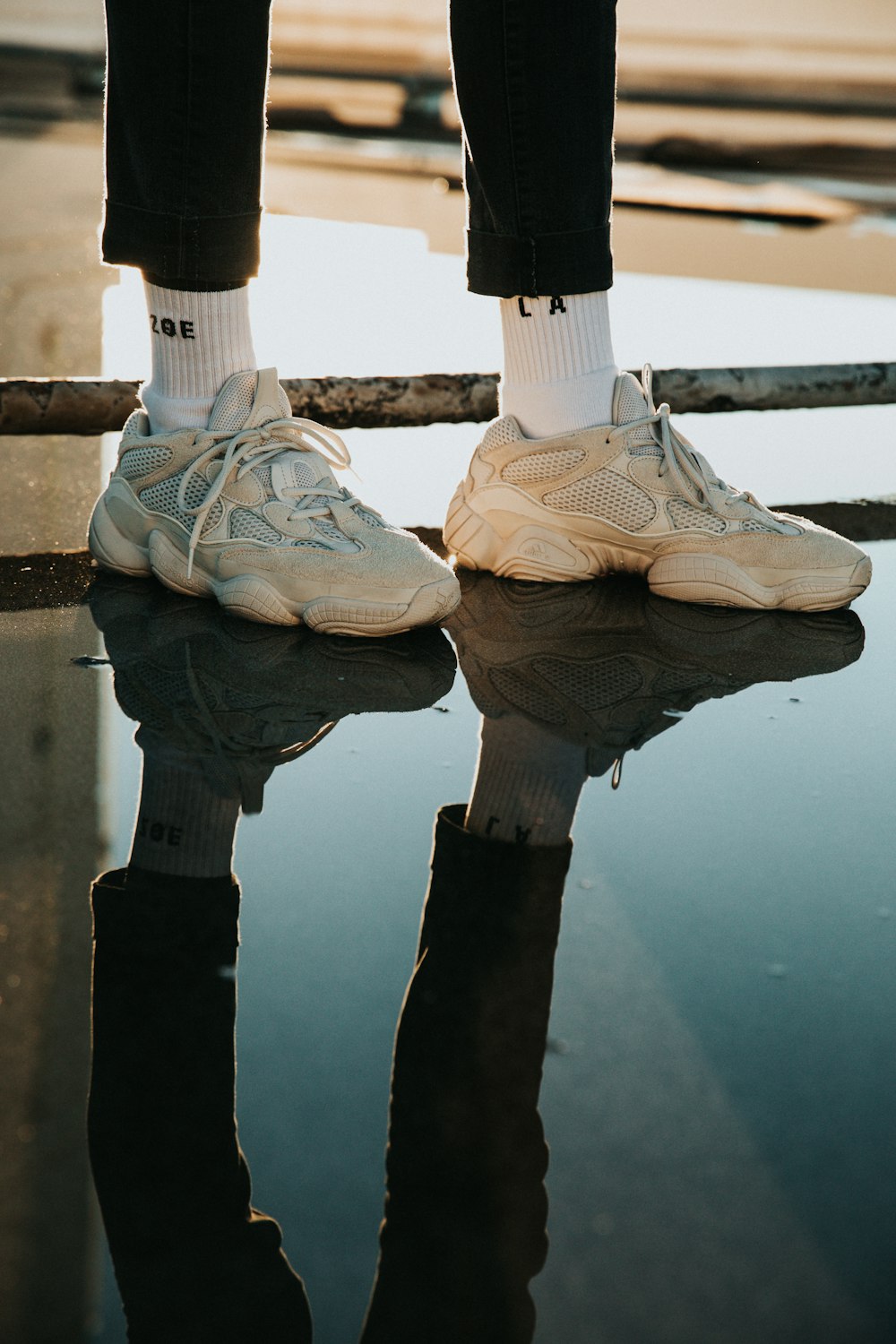 person wearing pair of white lace-up sneakers with reflection to water during daytime