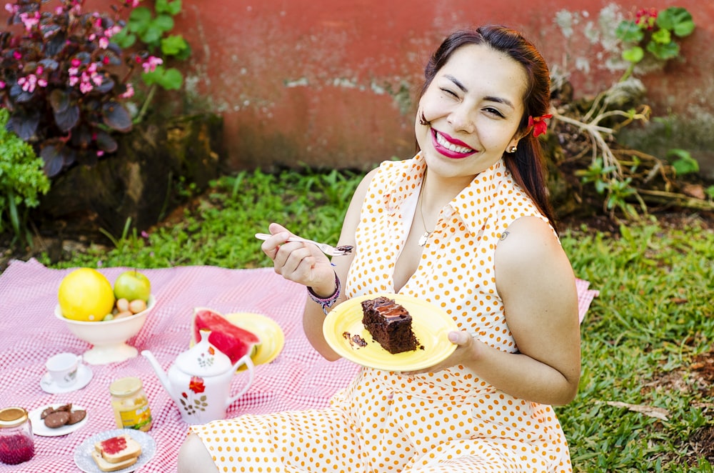 Femme en robe à pois tenant une fourchette et une assiette avec une tranche de gâteau