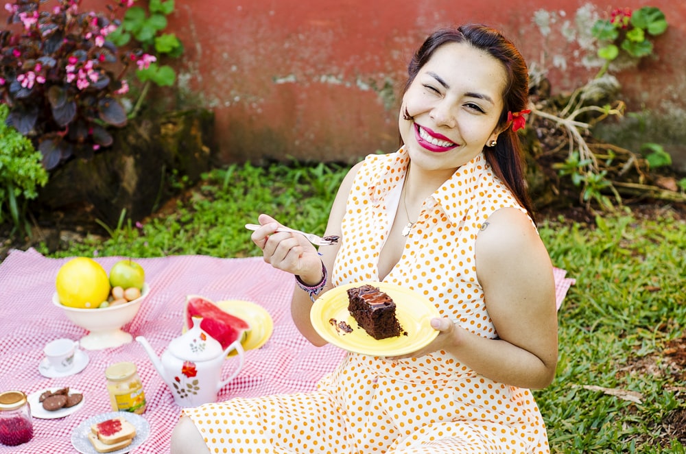 水玉模様のドレスを着た女性がフォークとケーキのスライスを持った皿を持っている