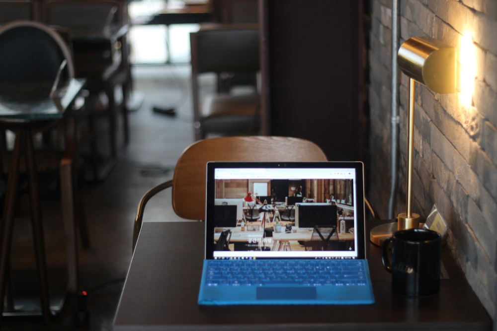 turned-on blue-and-black laptop computer near black ceramic mug on table