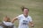 A female soccer player wearing a white jersey with 'Hoyas' and the number 23 printed on it is captured mid-motion, smiling with hair flying back. She appears to be on a grass field, engaging with someone in the foreground who wears a jacket with a fur collar.