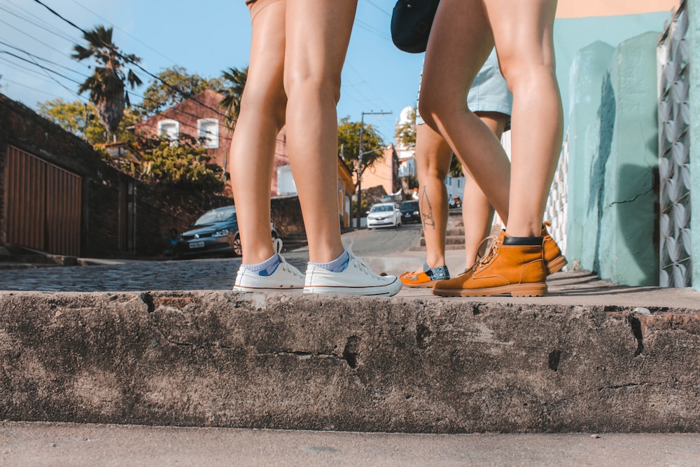 Mujer con un par de zapatillas blancas con cordones y otra mujer con botas de trabajo marrones durante el día