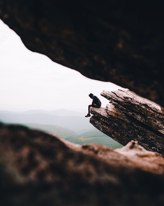 selective focus photography of person sitting on cliff during daytime in Hawksbill Mountain United States