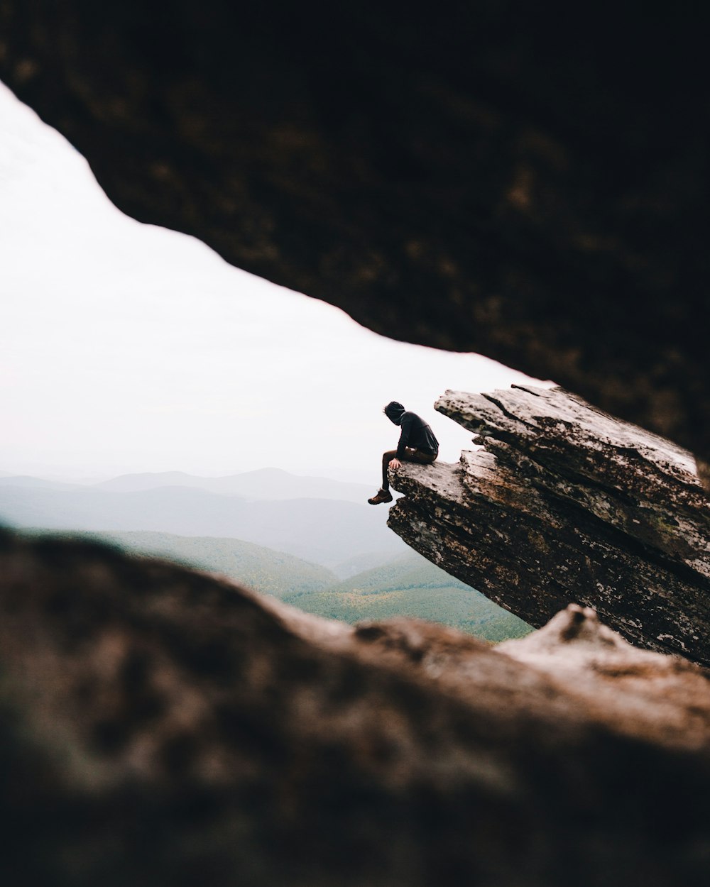 Selektive Fokusfotografie einer Person, die tagsüber auf einer Klippe sitzt