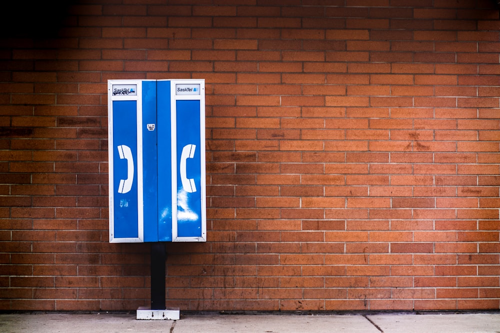 blue and white payphone near brown brick wall