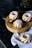 Four small bundt cakes with white icing are arranged on a wooden round board. One of the cakes is decorated with red berries. A small silver spoon is placed on the board. A light blue napkin is draped underneath the board and one cake rests on it.
