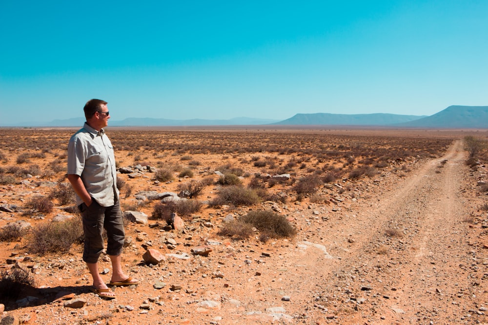 man wearing gray dress shirt and pants standing on dirt track during daytime