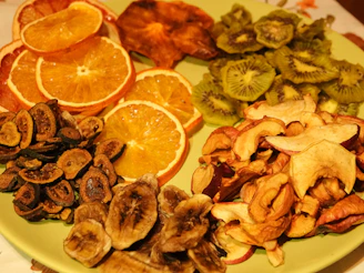 A plate filled with a colorful array of dried fruits, including orange slices, apple chips, kiwi slices, figs, banana chips, and sweet potato slices, all arranged in an appealing manner.