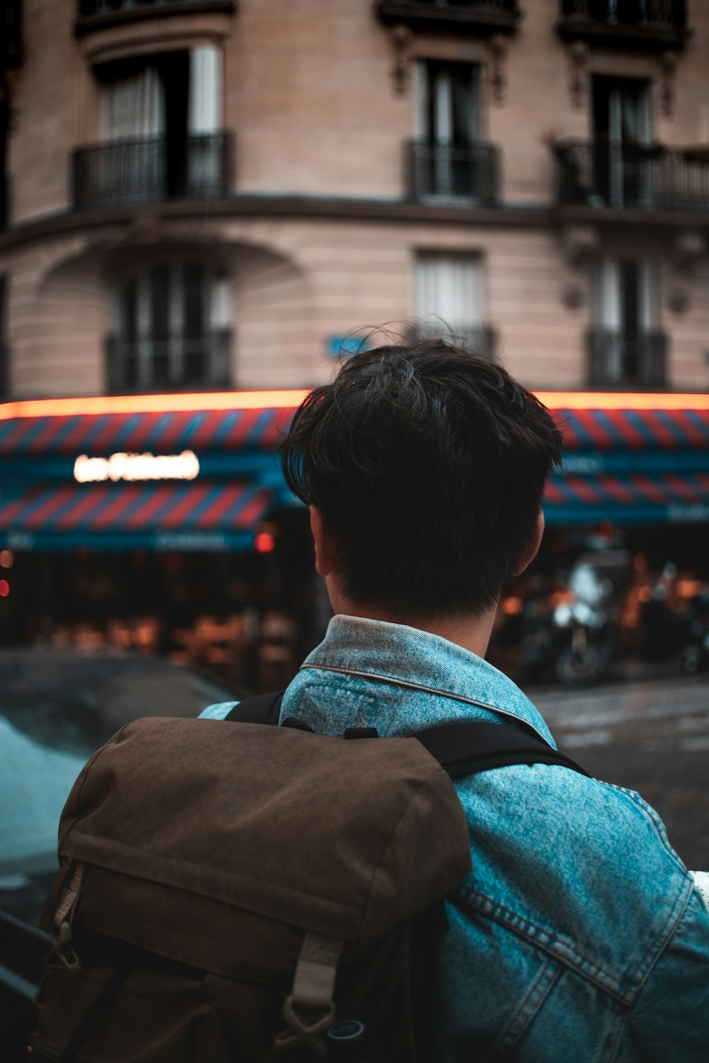 man wearing blue denim jacket and brown backpack