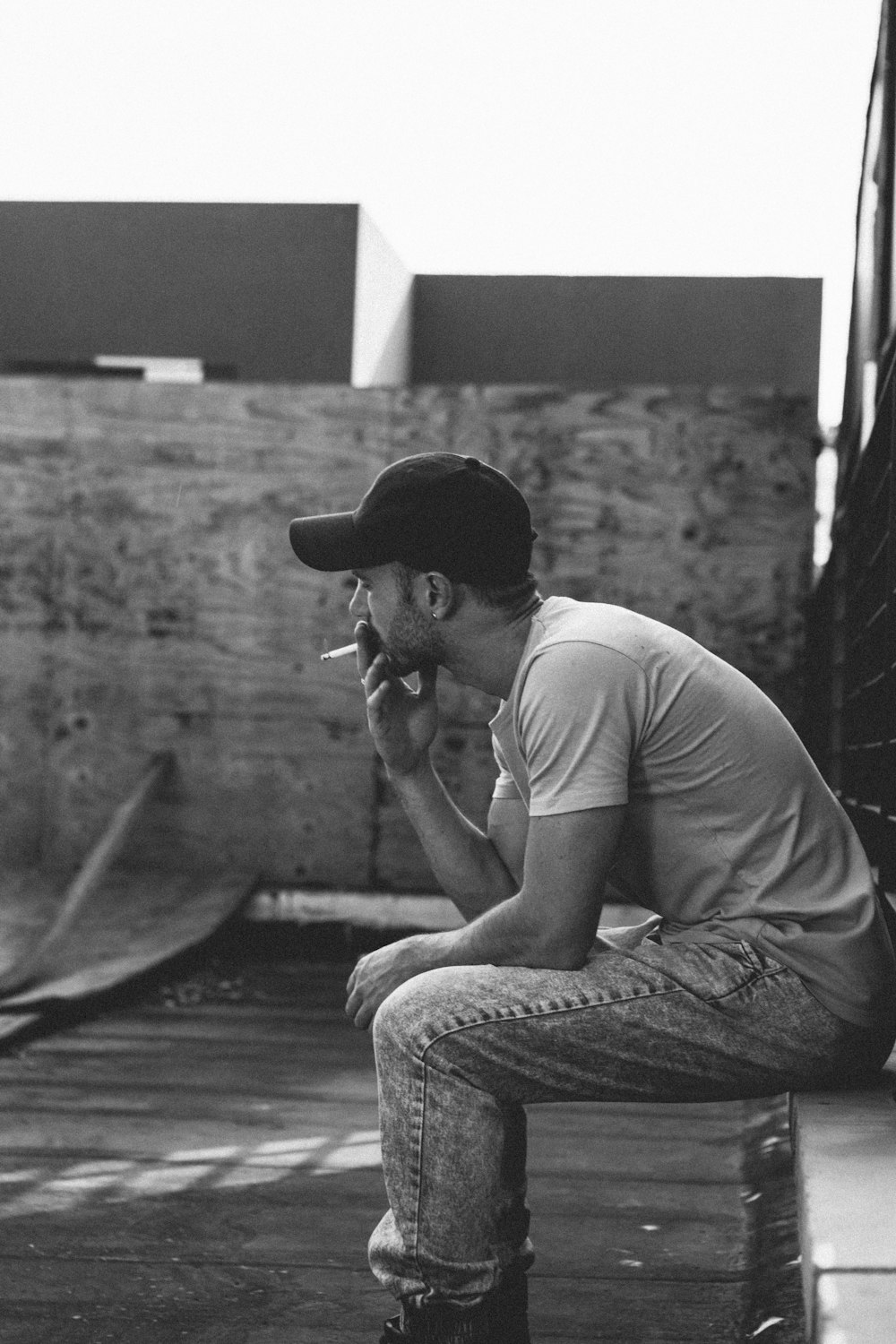 grayscale photography of man smoking while sitting on concrete wall