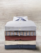 A neatly folded stack of casual men's shirts in soft, earthy tones.