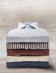 A neatly folded collection of men's shirts in neutral tones on a wooden table