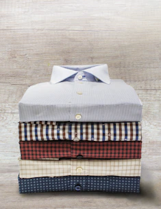 A neatly folded collection of men's shirts in neutral tones on a wooden table