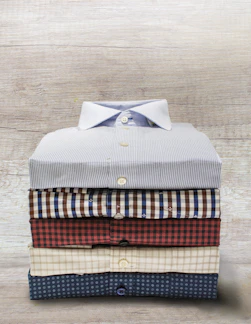 A neatly folded stack of crisp white chef uniforms on a wooden table.