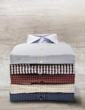 A neatly folded stack of casual men's shirts in soft, earthy tones.