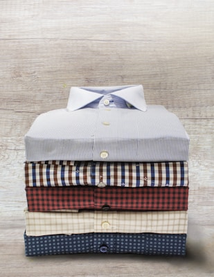A neatly folded stack of colorful men's casual shirts on a wooden table.