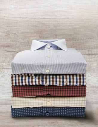 A neatly folded stack of school uniform shirts, ties, and sweaters on a wooden table.