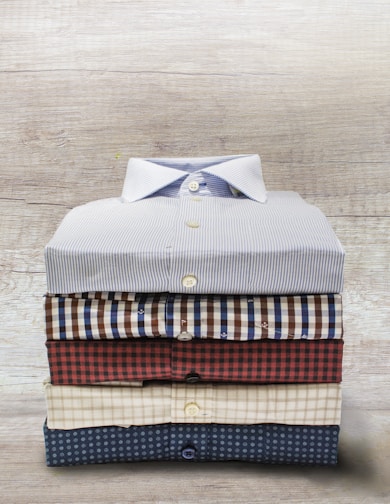 A neatly folded stack of soft, neutral-toned t-shirts with clean lines on a wooden surface.