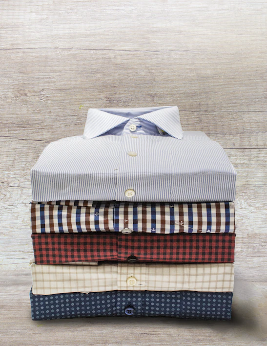 A neatly folded stack of crisp white chef uniforms on a wooden table.