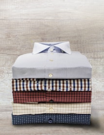 A neatly stacked set of five folded button-up shirts, each with different patterns and colors, arranged on a wooden surface.