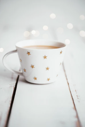 Close-up of a beige ceramic mug with a delicate golden print on a white background