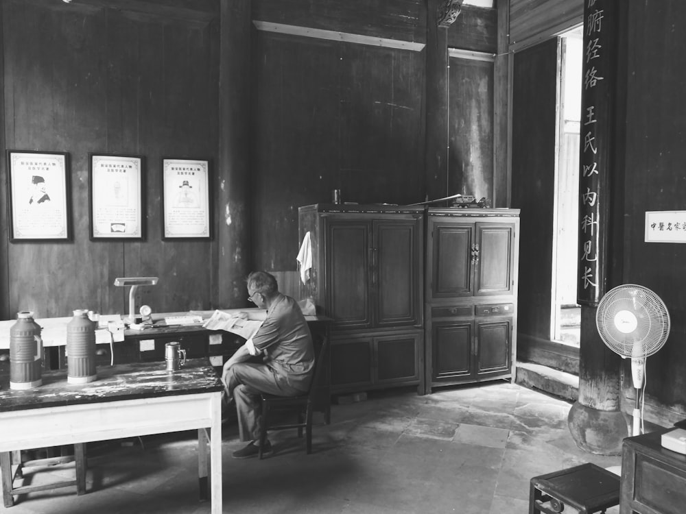 grayscale photo of man sitting on chair