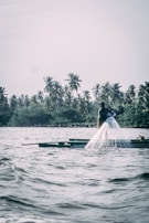 Fishermen casting nets into calm waters with boats in the background.