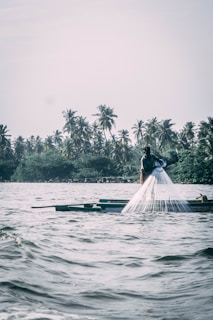 Fishermen casting nets into calm waters with boats in the background.