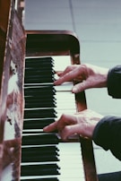Hands playing a piano, focusing on the keys and fingers in action. The wood of the piano and the contrast between the black and white keys create a classic, artistic atmosphere.