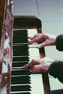 Hands playing a piano, focusing on the keys and fingers in action. The wood of the piano and the contrast between the black and white keys create a classic, artistic atmosphere.