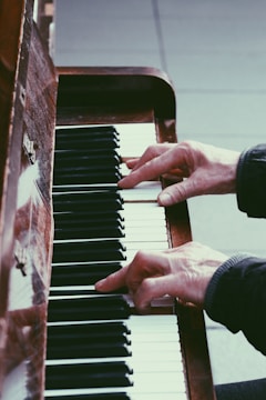 Hands playing a piano, focusing on the keys and fingers in action. The wood of the piano and the contrast between the black and white keys create a classic, artistic atmosphere.