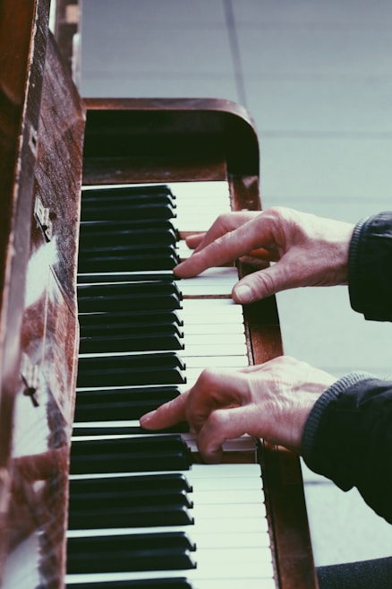 Hands playing a piano, focusing on the keys and fingers in action. The wood of the piano and the contrast between the black and white keys create a classic, artistic atmosphere.