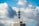 A telecommunications tower is mounted on top of a high-rise building. The sky is filled with large, fluffy clouds, giving a dynamic and textured backdrop.