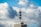 A telecommunications tower is mounted on top of a high-rise building. The sky is filled with large, fluffy clouds, giving a dynamic and textured backdrop.