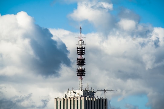 A telecommunications tower is mounted on top of a high-rise building. The sky is filled with large, fluffy clouds, giving a dynamic and textured backdrop.