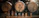Several beer bottles with colorful labels are displayed in front of large wooden barrels in a dimly lit brewery setting.