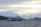 A cargo ship sails on a cold, choppy sea with snow-capped mountains in the background under a cloudy sky.