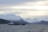 A cargo ship sails on a cold, choppy sea with snow-capped mountains in the background under a cloudy sky.