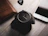 A sleek wristwatch resting on a wooden table beside a leather bag.