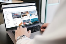 A person is using a laptop to browse an online marketplace featuring various digital products or themes. The screen displays a selection of software or website themes with descriptions and prices. The person seems to be in a well-lit room, sitting at a table.