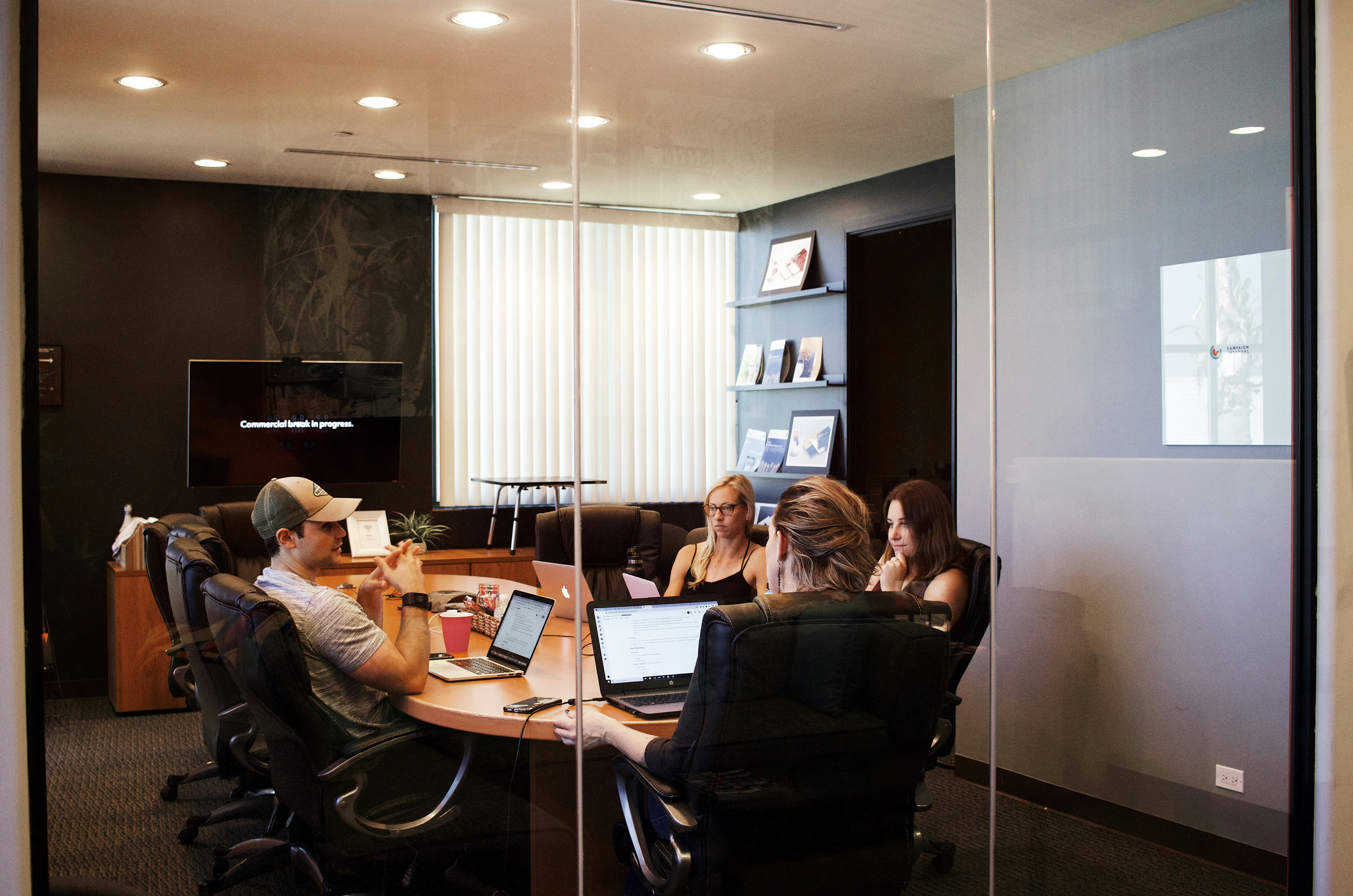 Group of people having a meeting in an office board room with laptops, audio systems and TV's