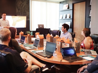 man standing in front of people sitting beside table with laptop computers