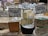 Various types of cheese are displayed on a counter in a market or store. Each cheese has a label with its name, origin, and price. The cheeses vary in color and texture, and the signs indicate different types of milk sources and flavor profiles.