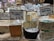 Various types of cheese are displayed on a counter in a market or store. Each cheese has a label with its name, origin, and price. The cheeses vary in color and texture, and the signs indicate different types of milk sources and flavor profiles.