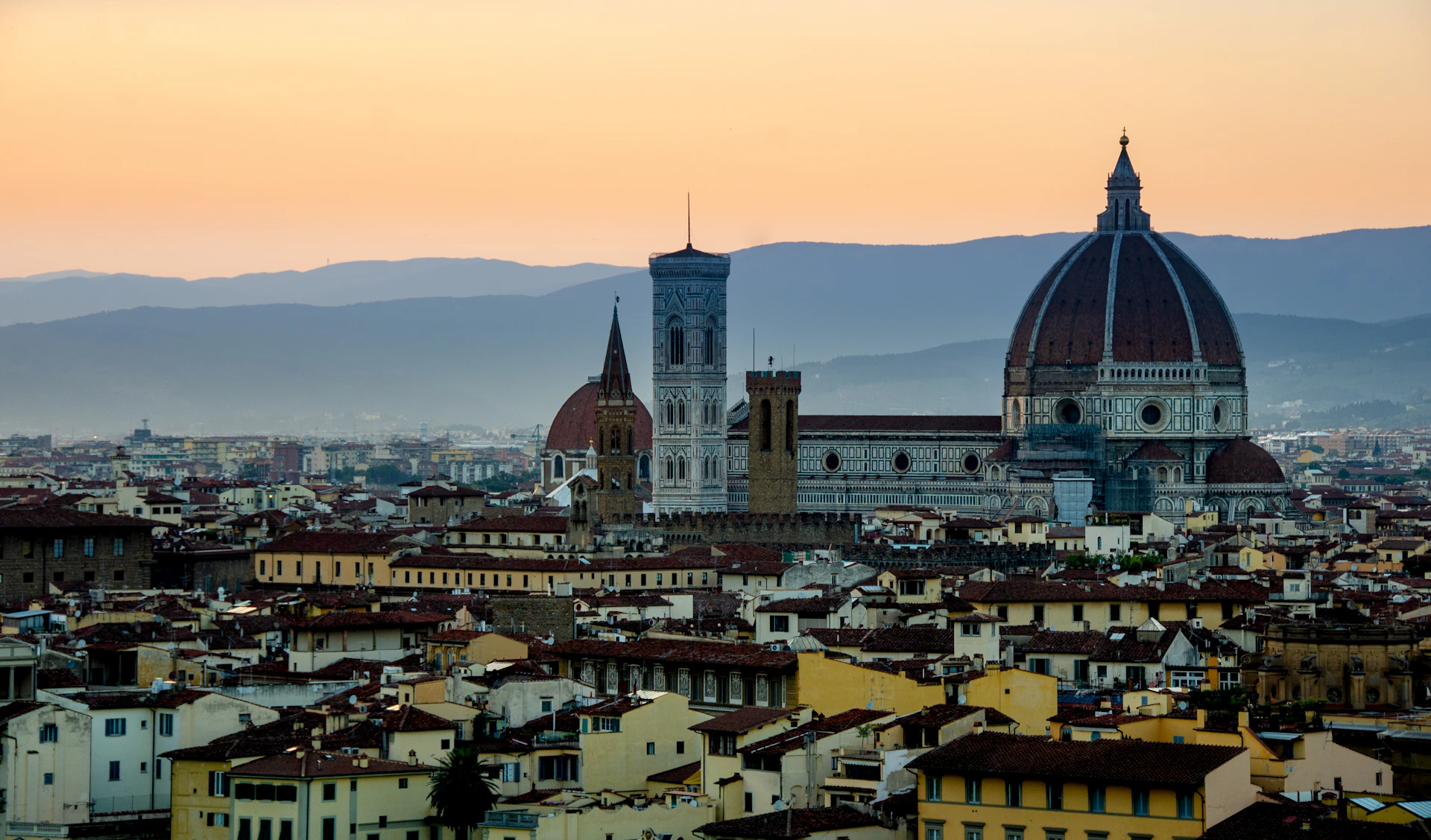 A stunning view of the medieval skyline of Assisi at sunset, with the Basilica of Saint Francis glowing warmly in the fading light.