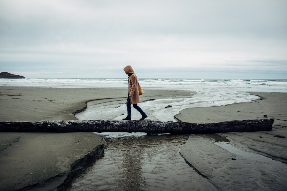 person walking along tree trunk used as bridge