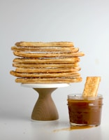 A stack of golden sweet pastries dusted lightly with powdered sugar on a beige linen cloth.