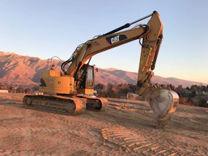 A sturdy excavator parked on a construction site with mountains in the background