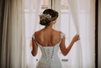 woman in wedding dress standing near window looking outside while holding the curtains