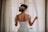 woman in wedding dress standing near window looking outside while holding the curtains